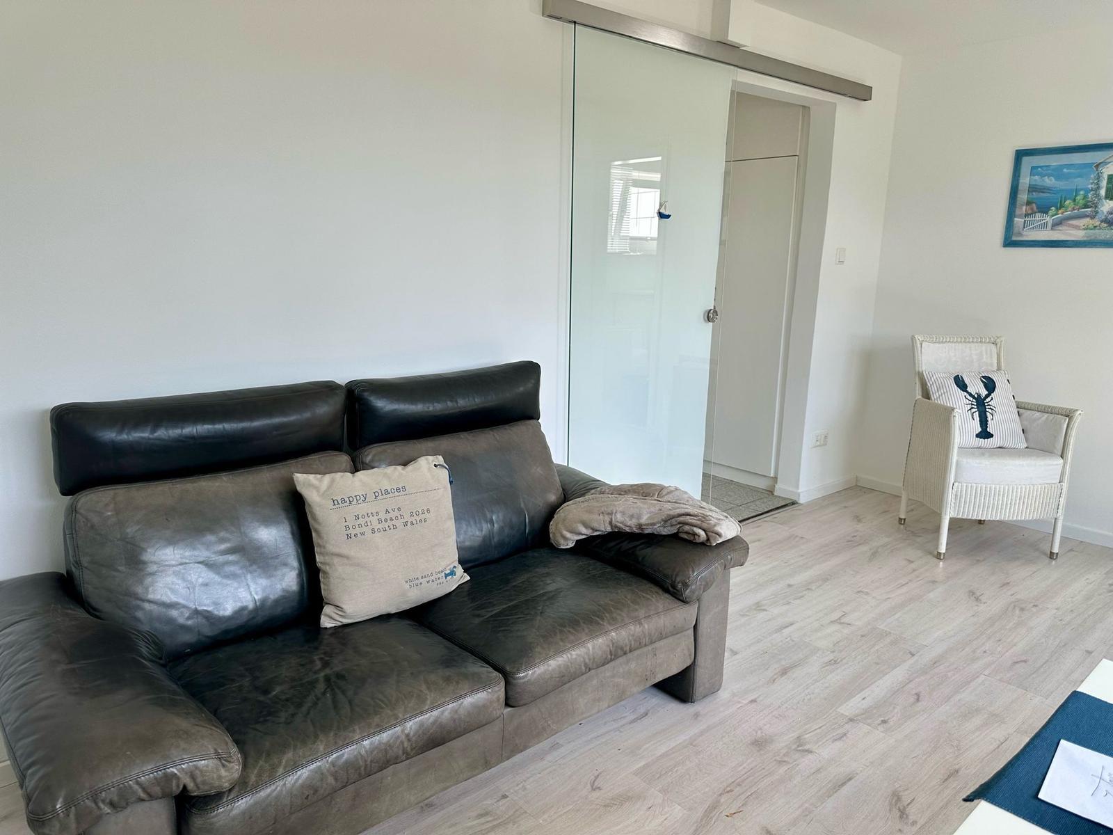 Ein Wohnzimmer mit Ledersofa, weiße Sitzgelegenheit und Glaswand.