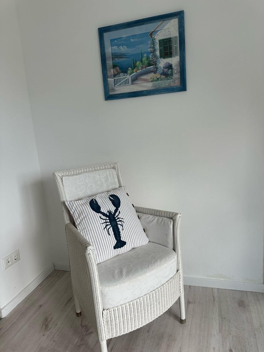 Weißer Rattan-Stuhl mit Kissen und Wandbild an der Wand.