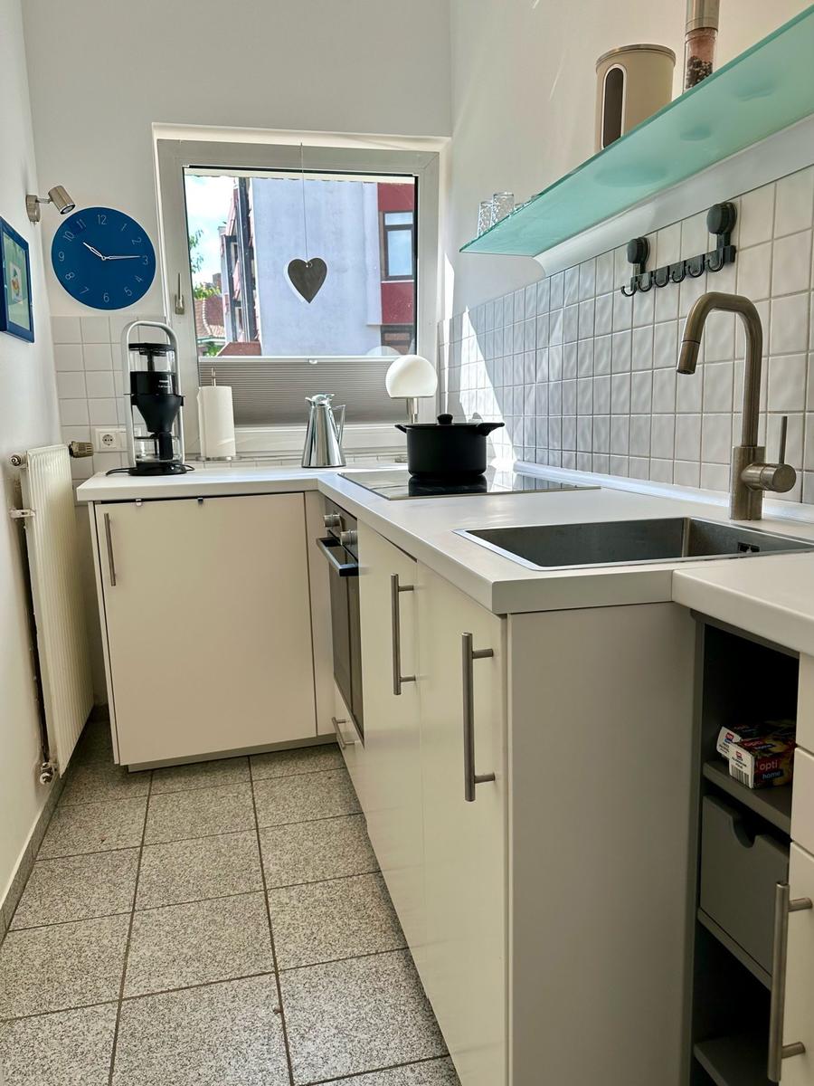 Küche mit weißen Schränken, Edelstahlspüle und Fenster mit Herz.