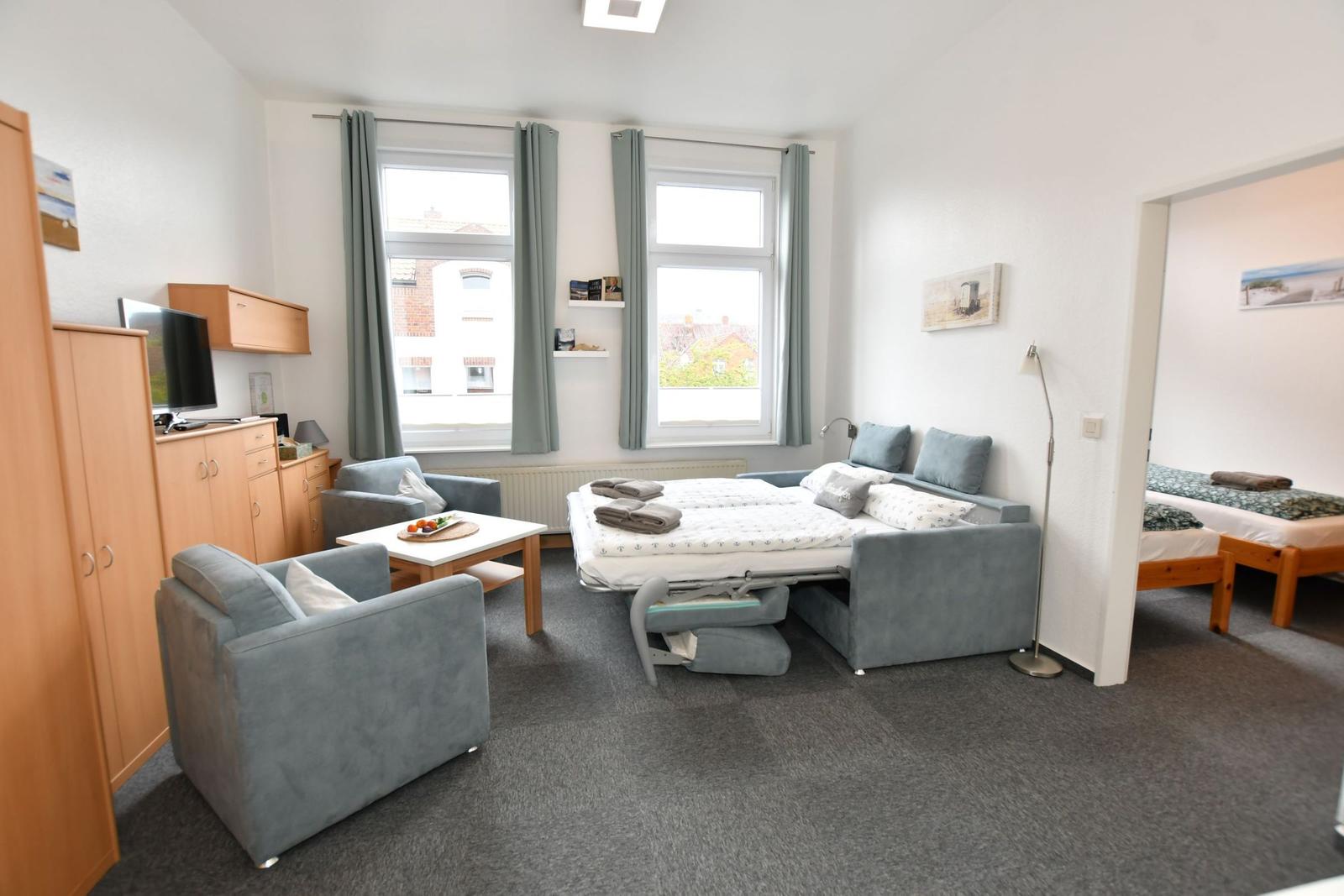 Zimmer mit Schlafcouch, Sitzgelegenheiten und Fenstern mit Blick.