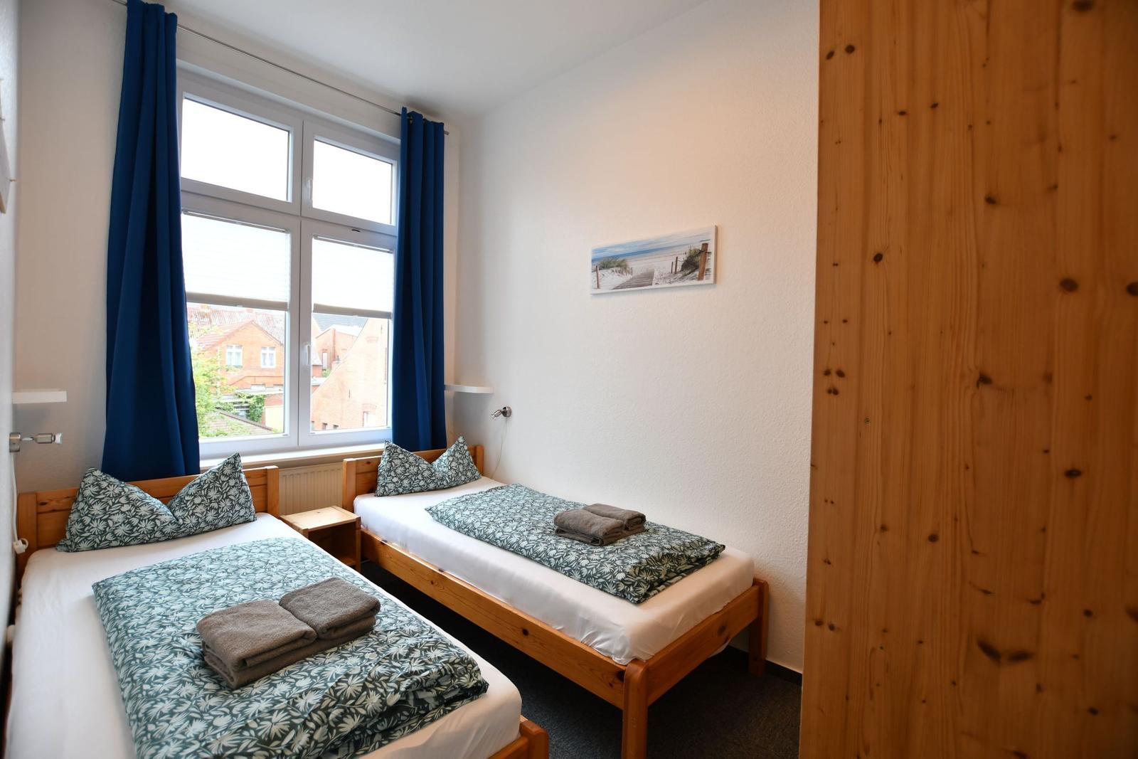 Zwei Einzelbetten mit Bettwäsche, Fenster mit blauen Vorhängen und Holzwand.