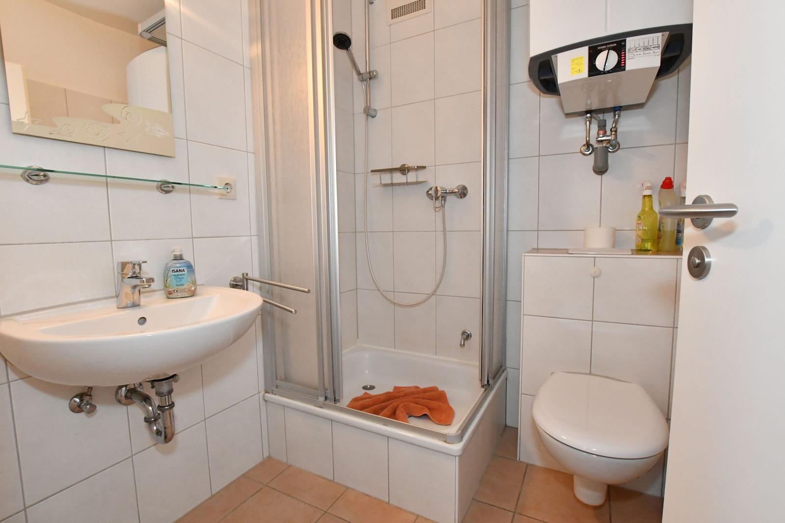 Badezimmer mit Dusche, Waschbecken und Toilette. Orange Handtuch liegt in der Dusche.