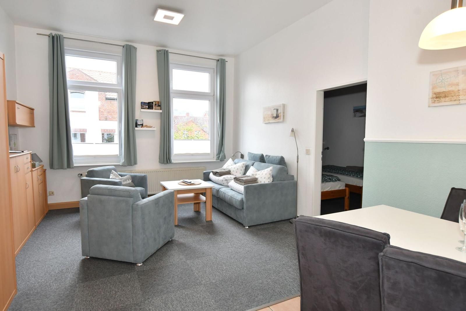 Wohnzimmer mit Sofa, Sesseln und Essbereich. Blick auf Schlafzimmer.