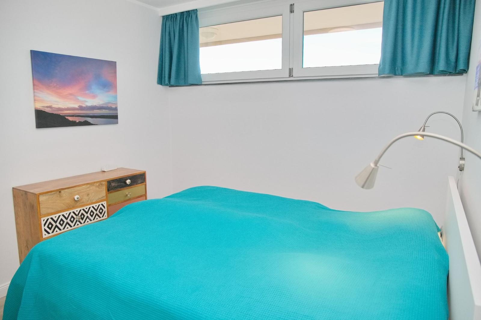 Schlafzimmer mit Bett, Schrank und Fenster mit Vorhängen.