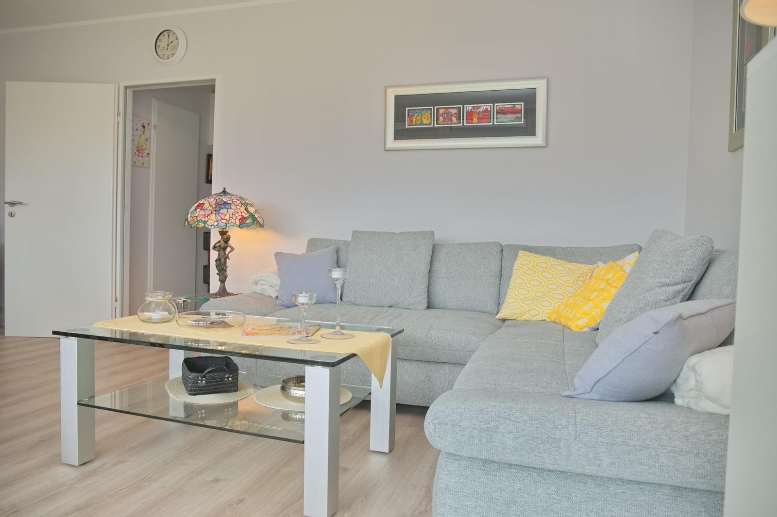 Wohnzimmer mit grauem Sofa, Glas-Tisch und Stehlampe.