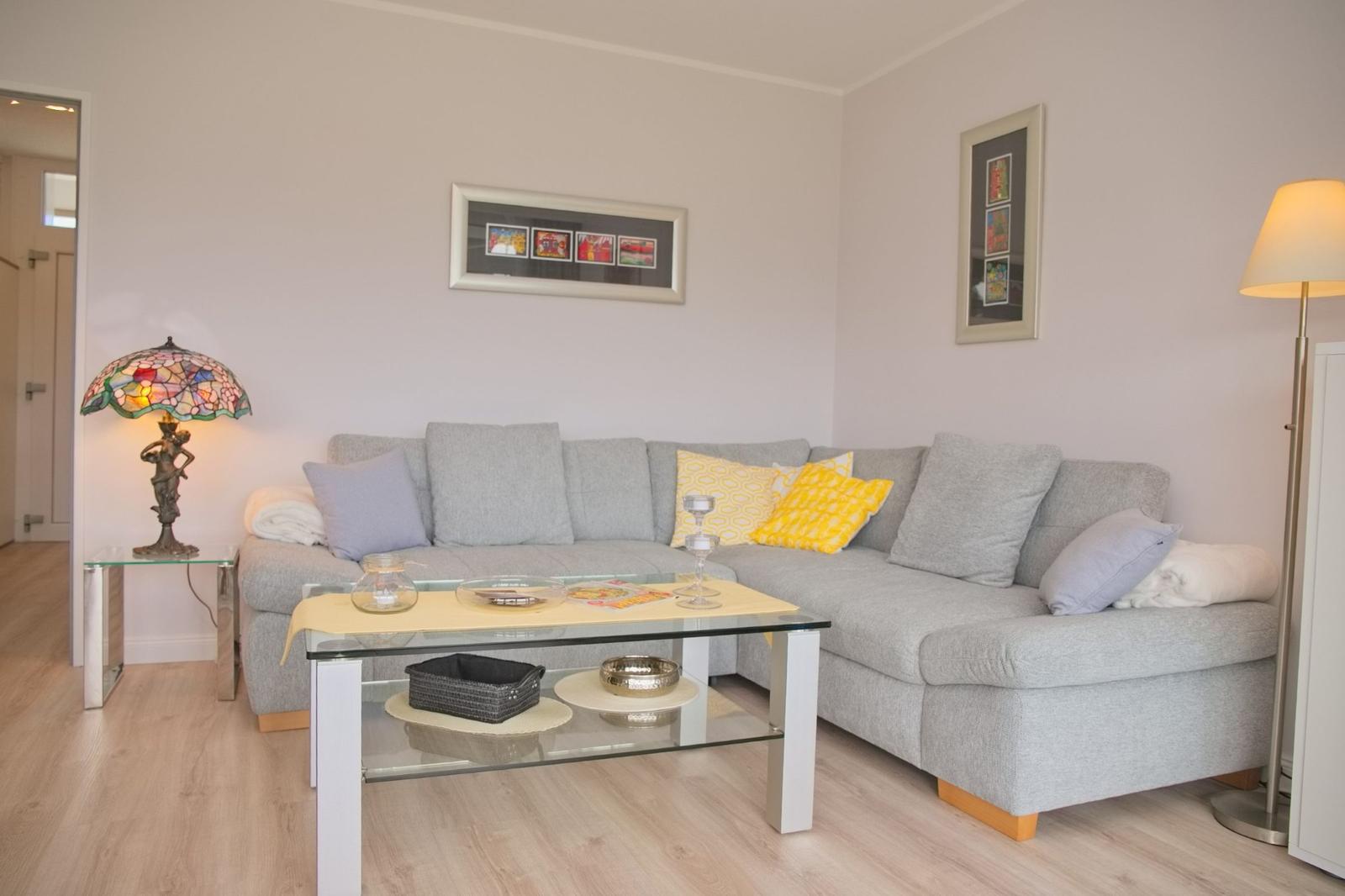 Ein Wohnzimmer mit grauem Sofa, Glas-Tisch und Stehlampe.