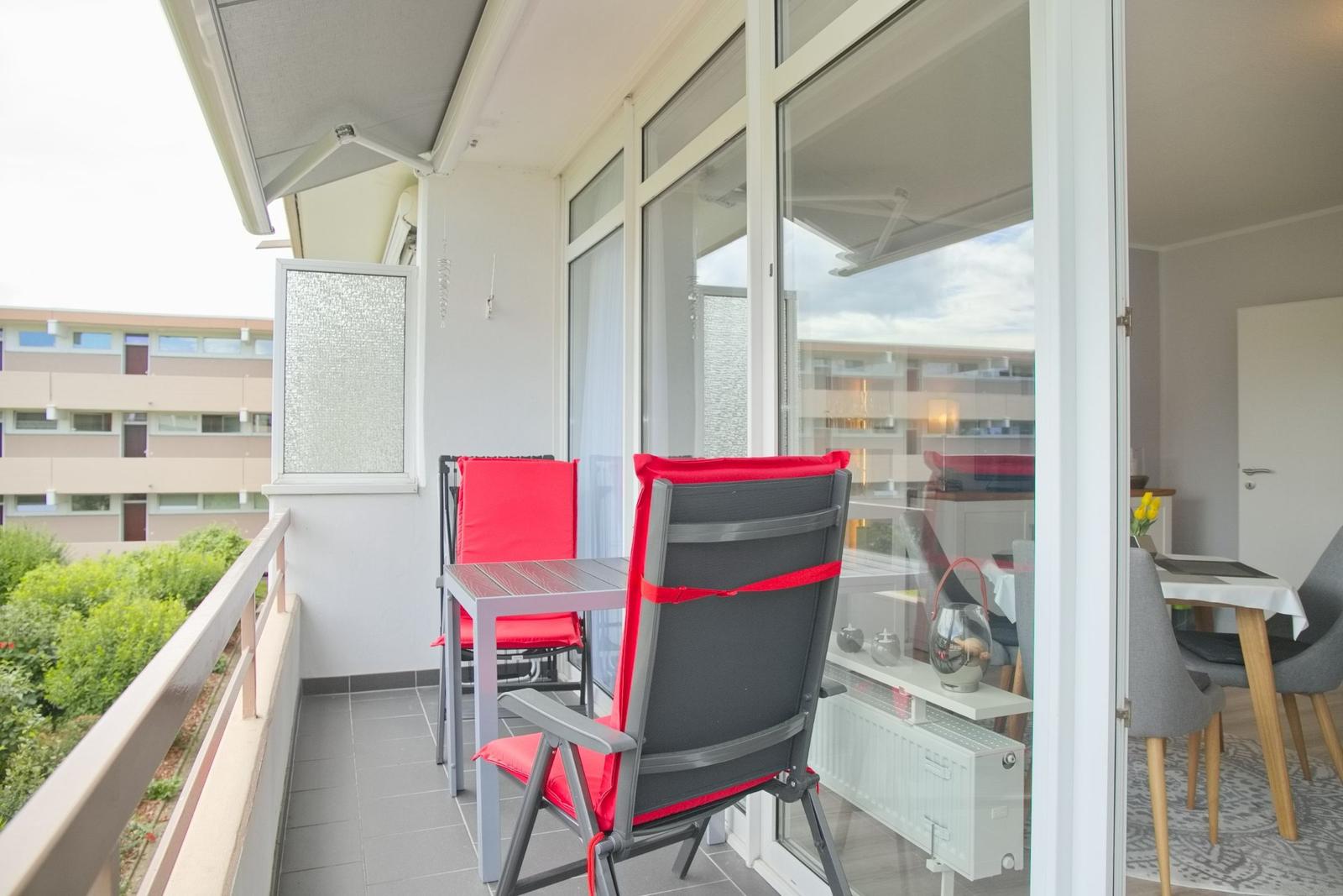 Terrasse mit Tisch, zwei roten Stühlen und Blick auf Wohnbereich.