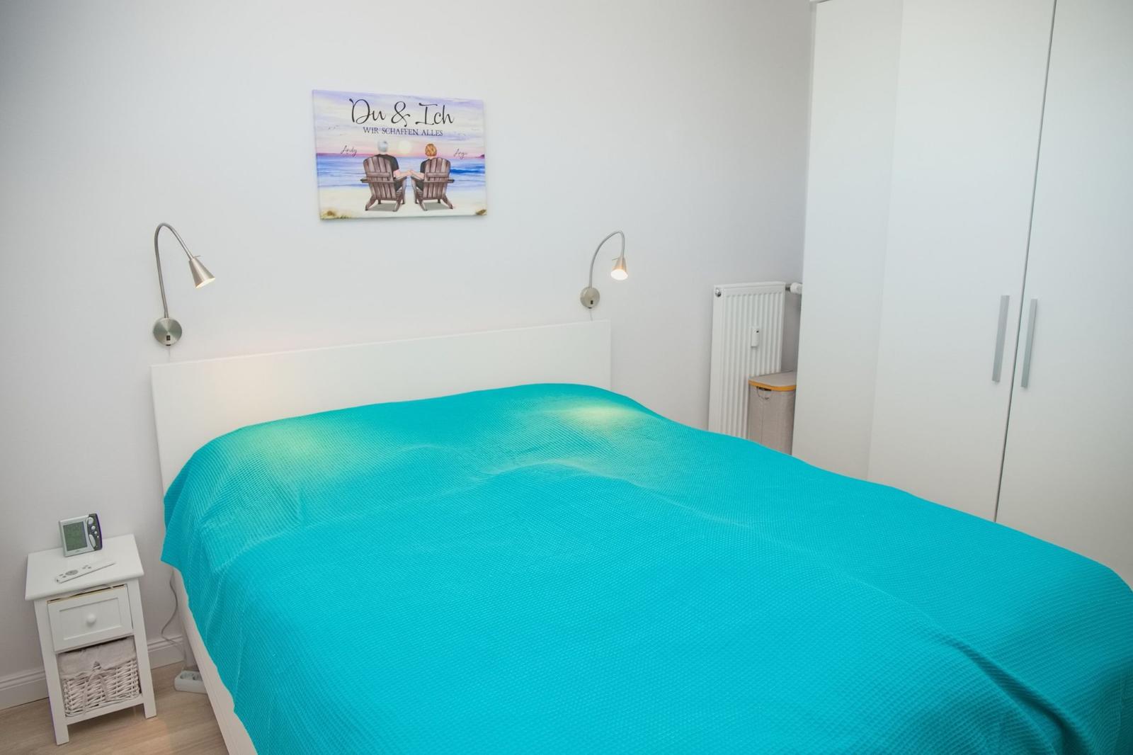 Schlafzimmer mit Bett, Nachttisch und Kleiderschrank. Wandbild und Stehlampe.