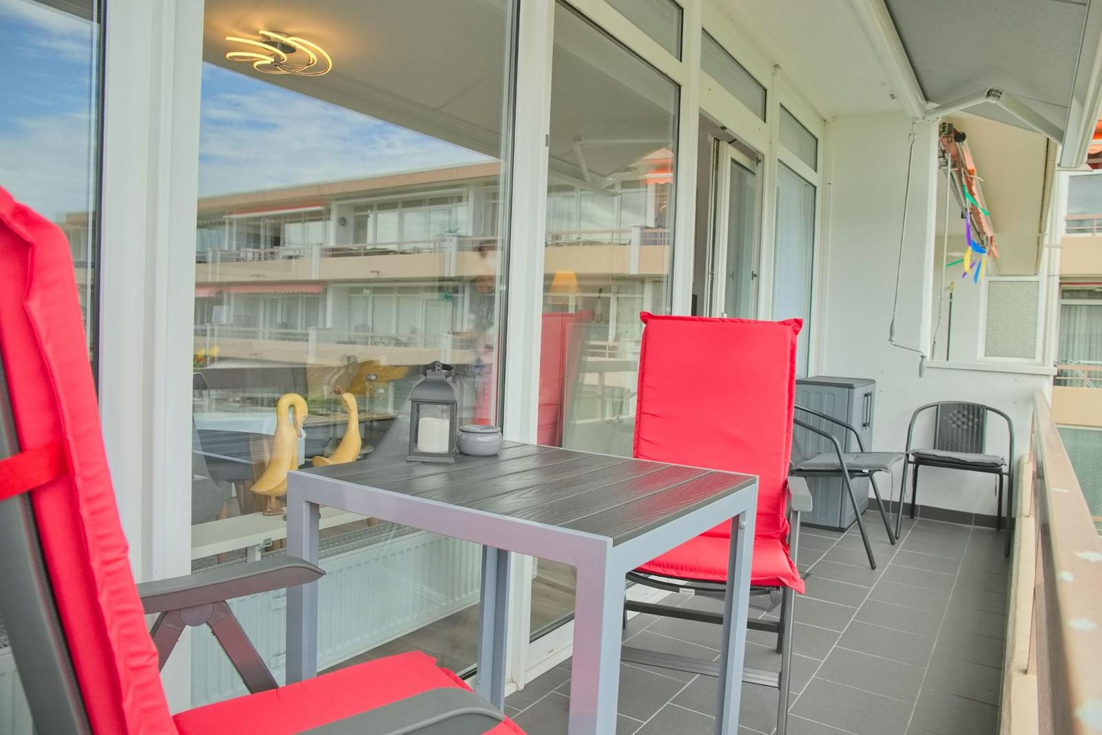 Terrasse mit Tisch, zwei roten Stühlen und Blick auf Gebäude.
