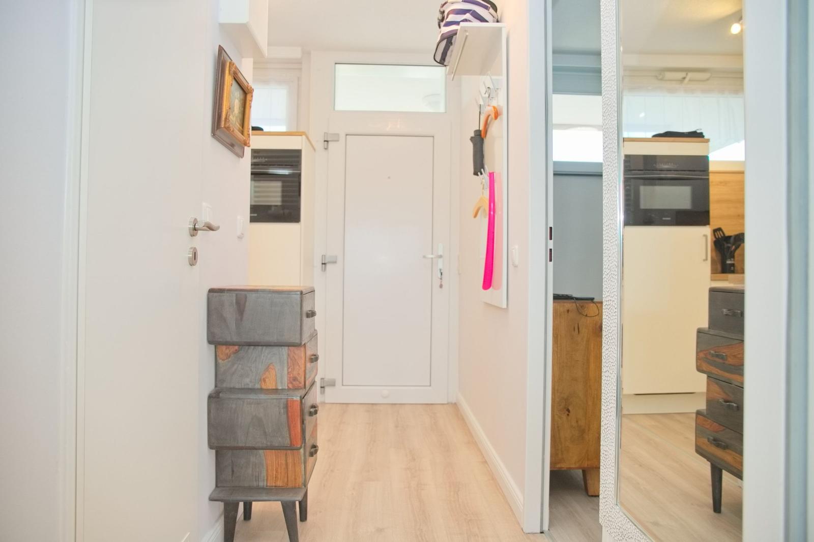 Flur mit Garderobe, Spiegel und Küchenbereich im Hintergrund.