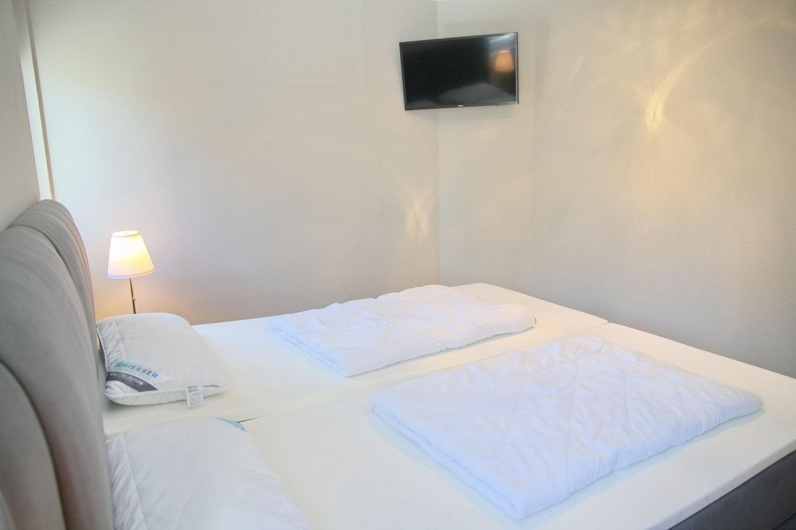 Schlafzimmer mit Bett, Lampe und Wandfernseher.