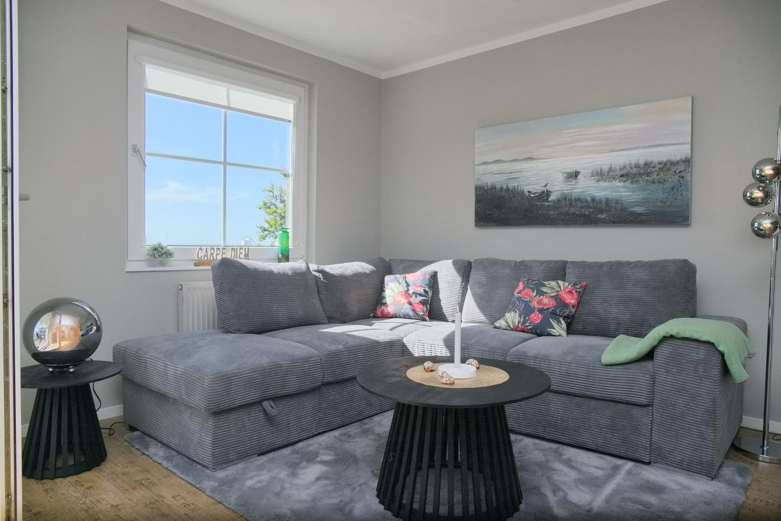 Ein Wohnzimmer mit grauem Sofa, runden Tischen und Wandbild.