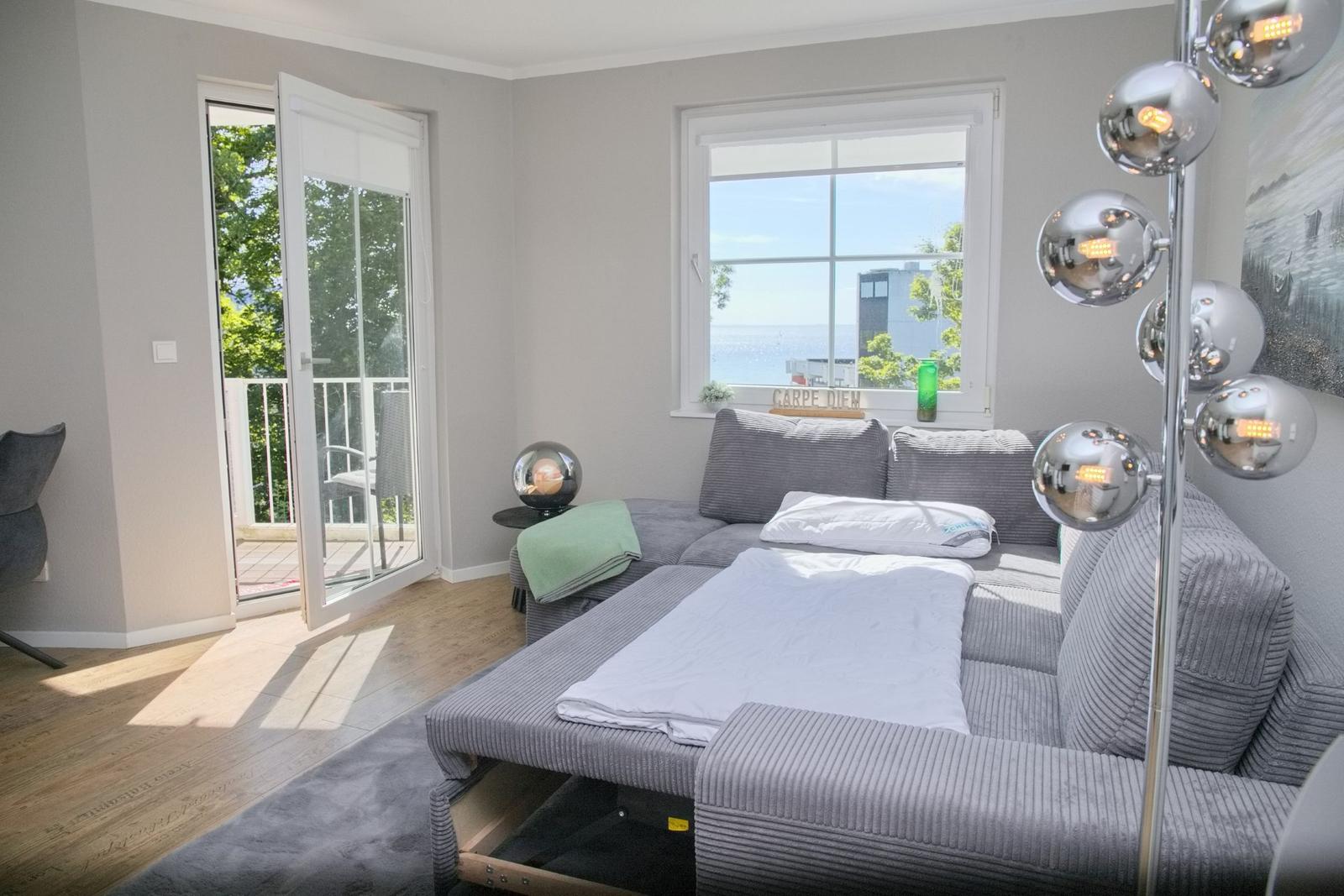 Ein Wohnzimmer mit Sofa, Balkon und Meerblick durch Fenster.