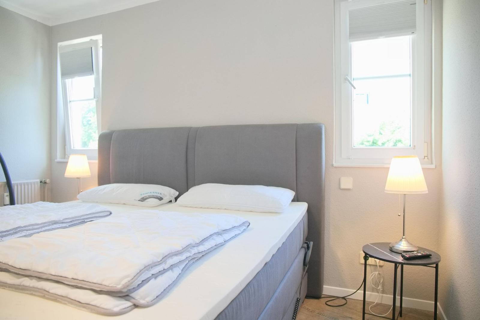 Schlafzimmer mit Bett, zwei Fenstern und Nachttischen mit Lampen.