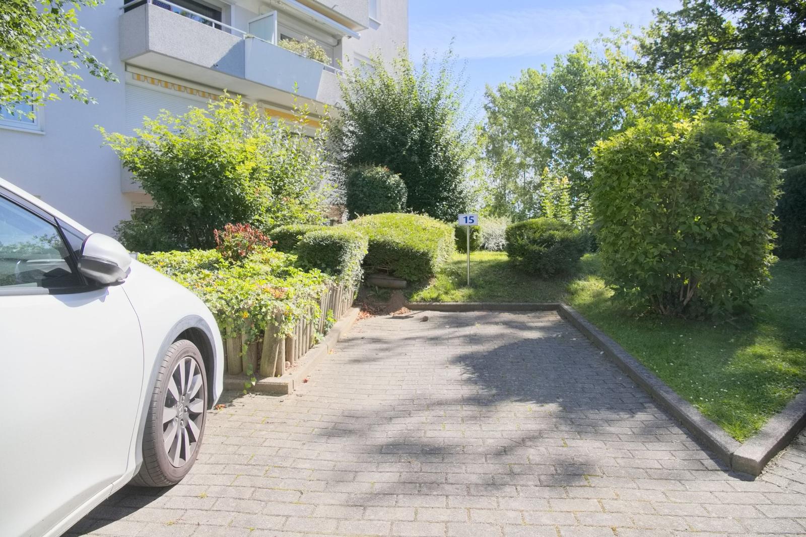 Pflasterweg führt zu einer Wohnung mit Garten und Parkplatz. Ein weißes Auto steht bereit.