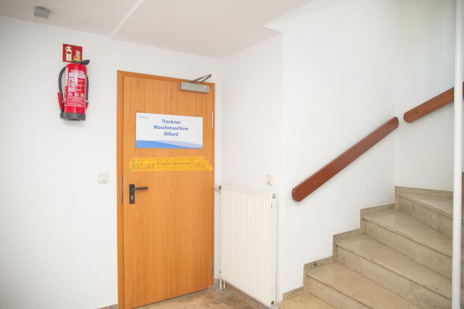 Trockner, Waschmaschine und Billard hinter Tür. Treppenhaus mit Holzgeländer.