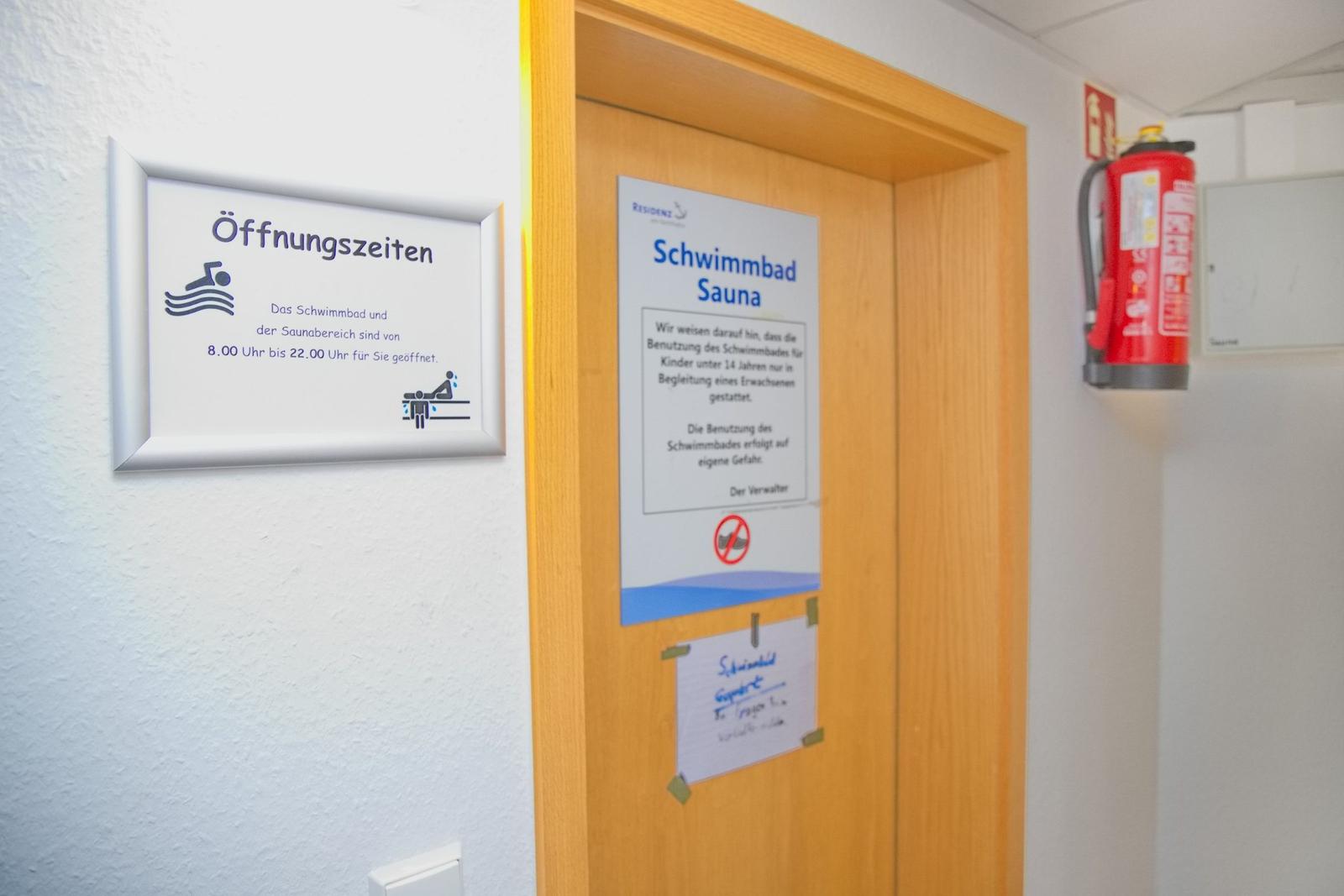Türe zum Schwimmbad und Sauna mit Öffnungszeiten und Sicherheitsausrüstung.