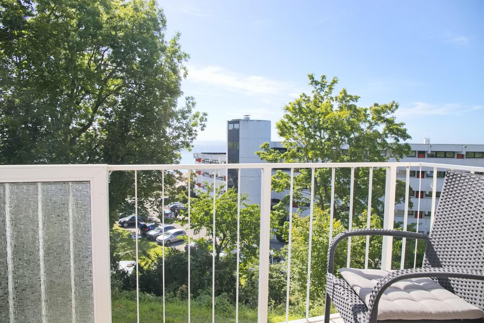 Terrasse mit Sitzgelegenheit und Blick auf Grünflächen und Gebäude.