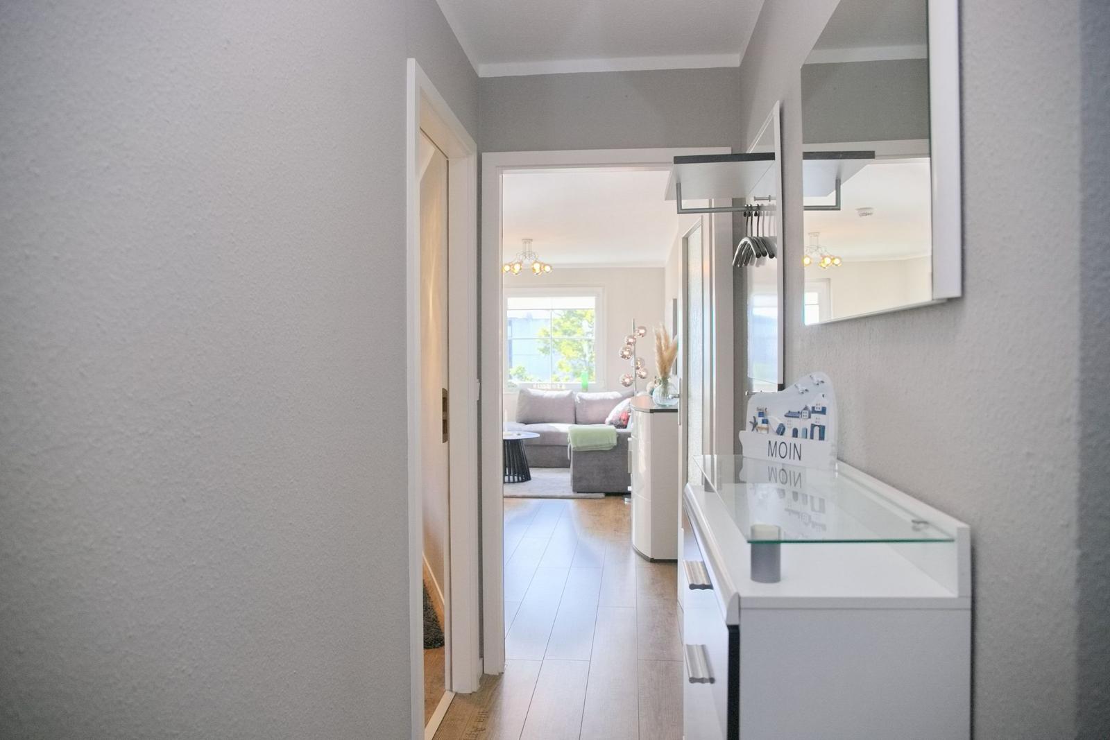 Flur mit Spiegelschrank und Blick in Wohnzimmer mit Sofa und Fenster.