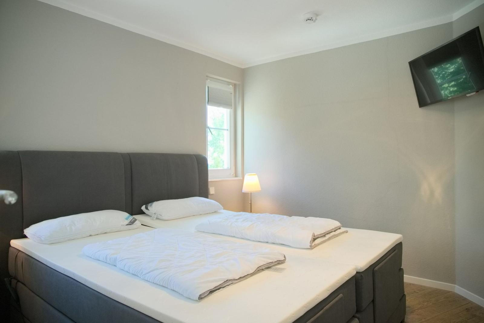 Zimmer mit Doppelbett, Fenster und Wandfernseher.