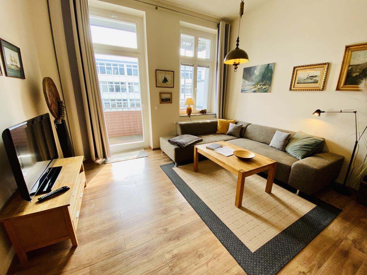 Wohnzimmer mit Sofa, Couchtisch und Fernseher. Fenster mit Blick auf Balkon.