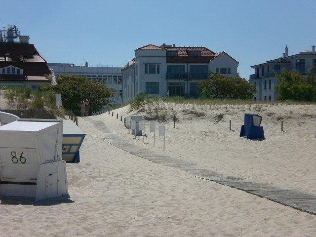 Sandy beach path with wooden walkway, beach chairs, and buildings in background.