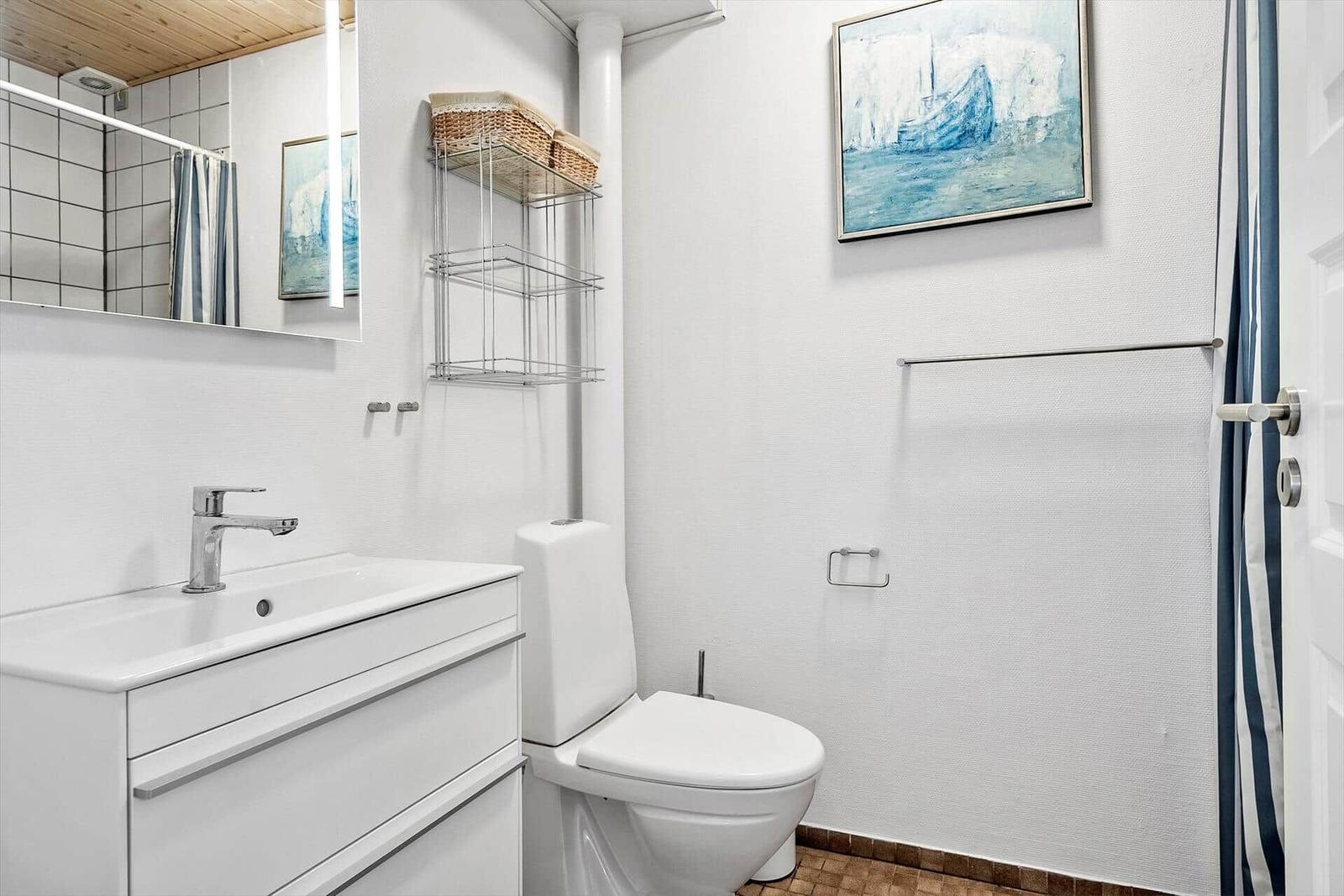 Badezimmer mit Waschbecken, Toilette und Dusche. Wandbild und Spiegel sichtbar.