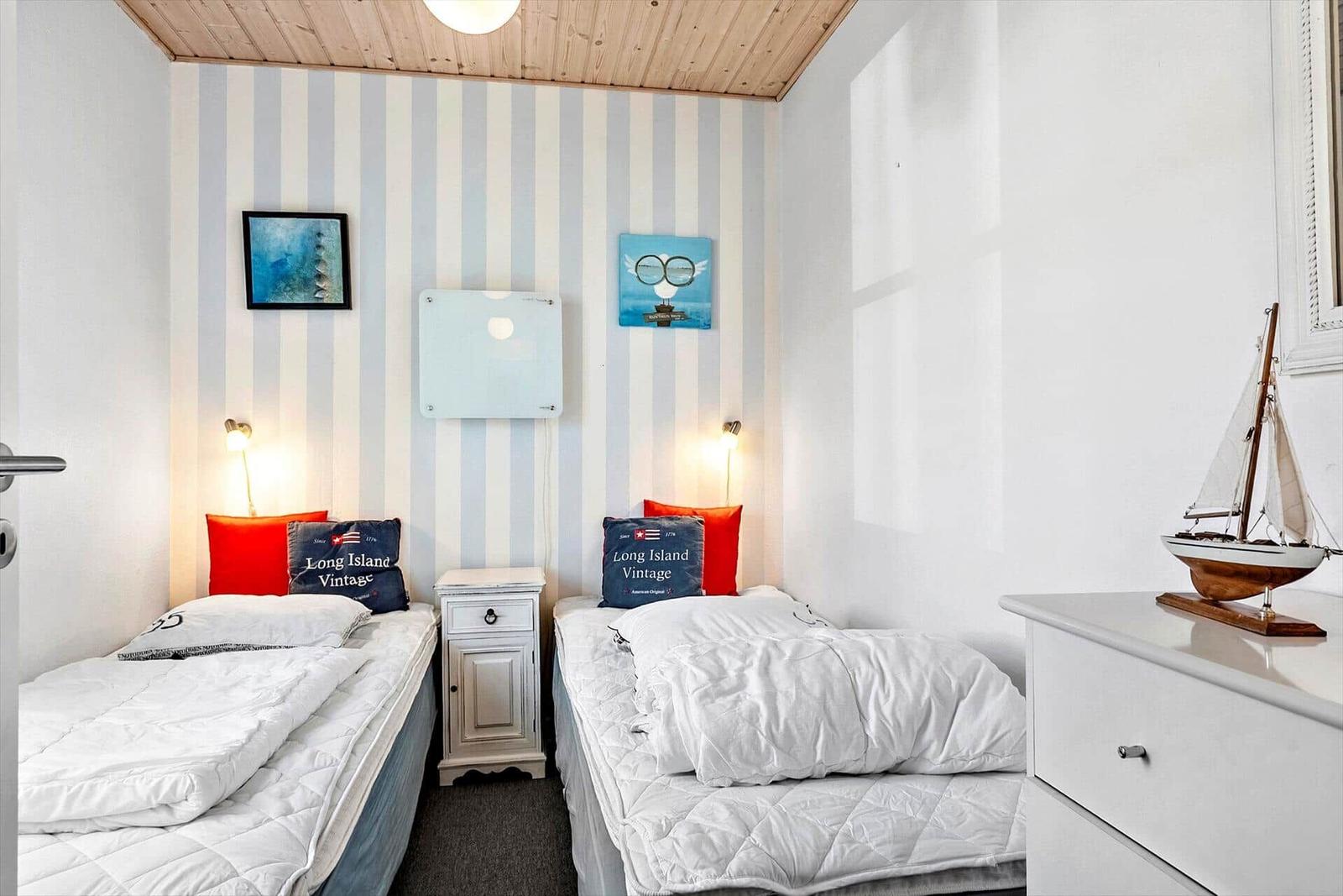 Zwei Betten mit weißen Bettwäschen, gestreifter Wand und Modellboot.