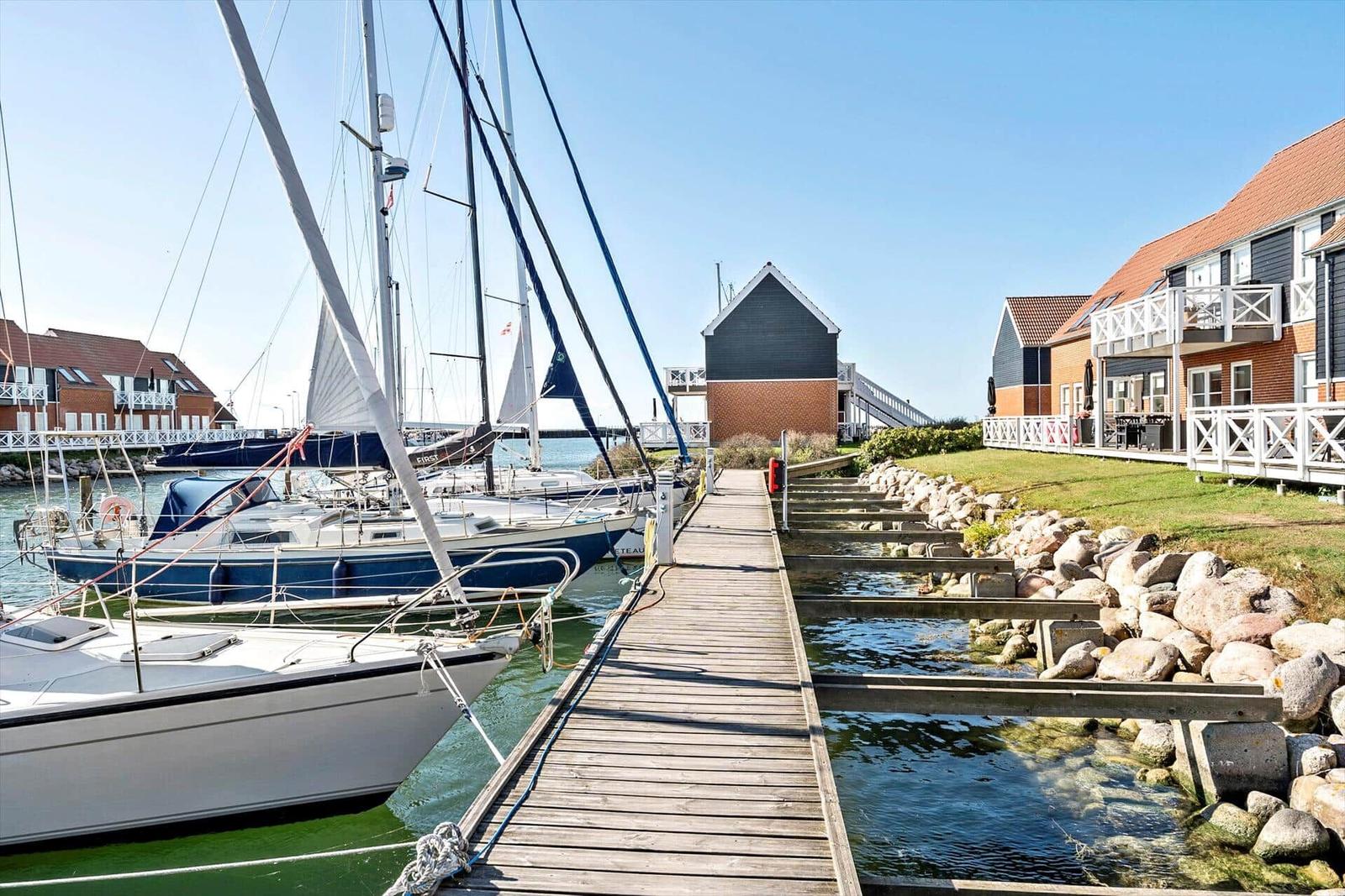 Holzsteg führt zu Booten im Hafen mit Häusern am Ufer.