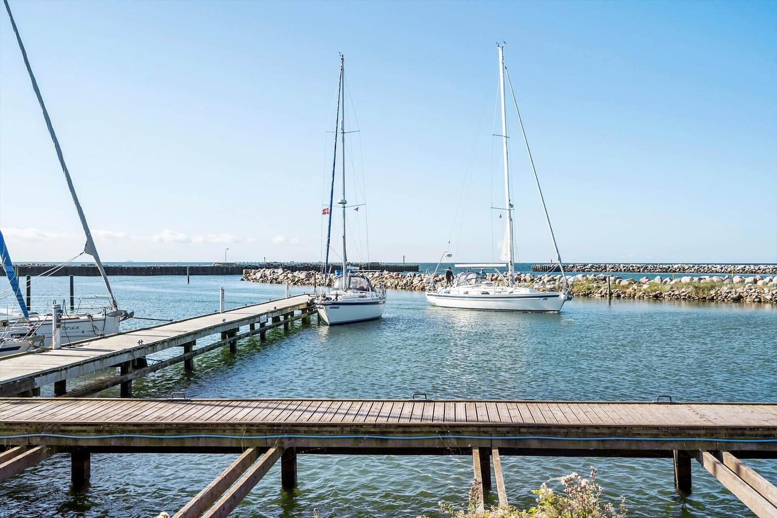 Hafen mit zwei Segelyachten und hölzernem Steg im Hintergrund.