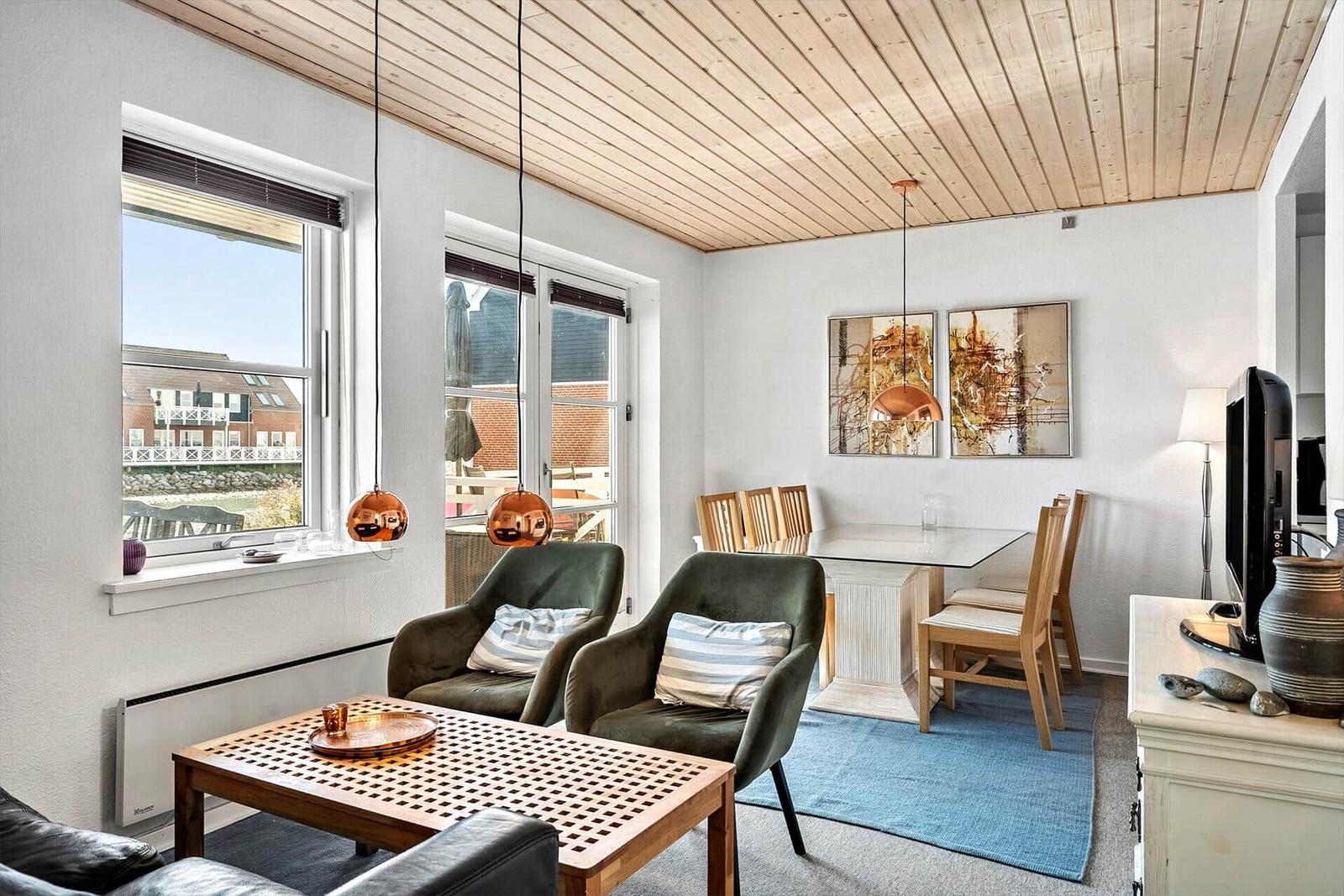 Wohn- und Essbereich mit Holzdecke, zwei grünen Sesseln und Essgruppe.