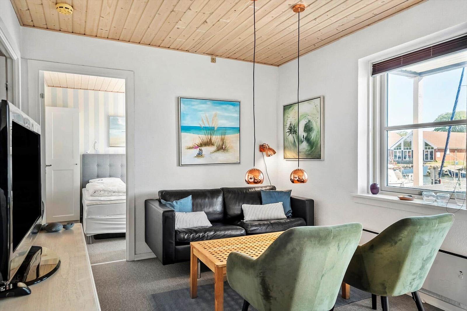 Wohnzimmer mit Sofa, zwei Sesseln und Blick auf Hafen. Schlafzimmer im Hintergrund.