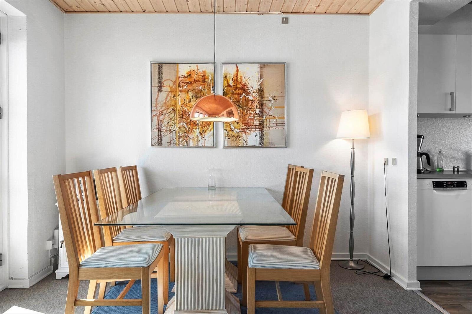 Essbereich mit Glasplatte, Holzstühlen und Wandbildern.