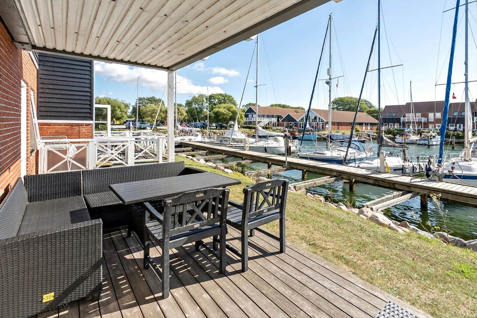 Terrasse mit Sitzgruppe überblickt einen Bootssteg mit Segelbooten.