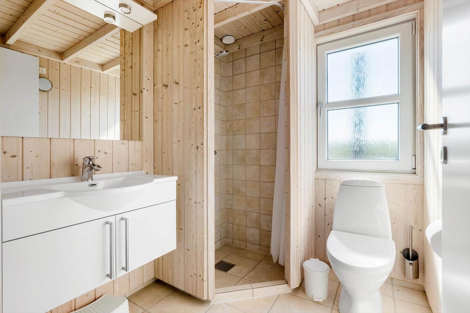 Badezimmer mit Dusche, Toilette und Waschbecken an Holzwänden.