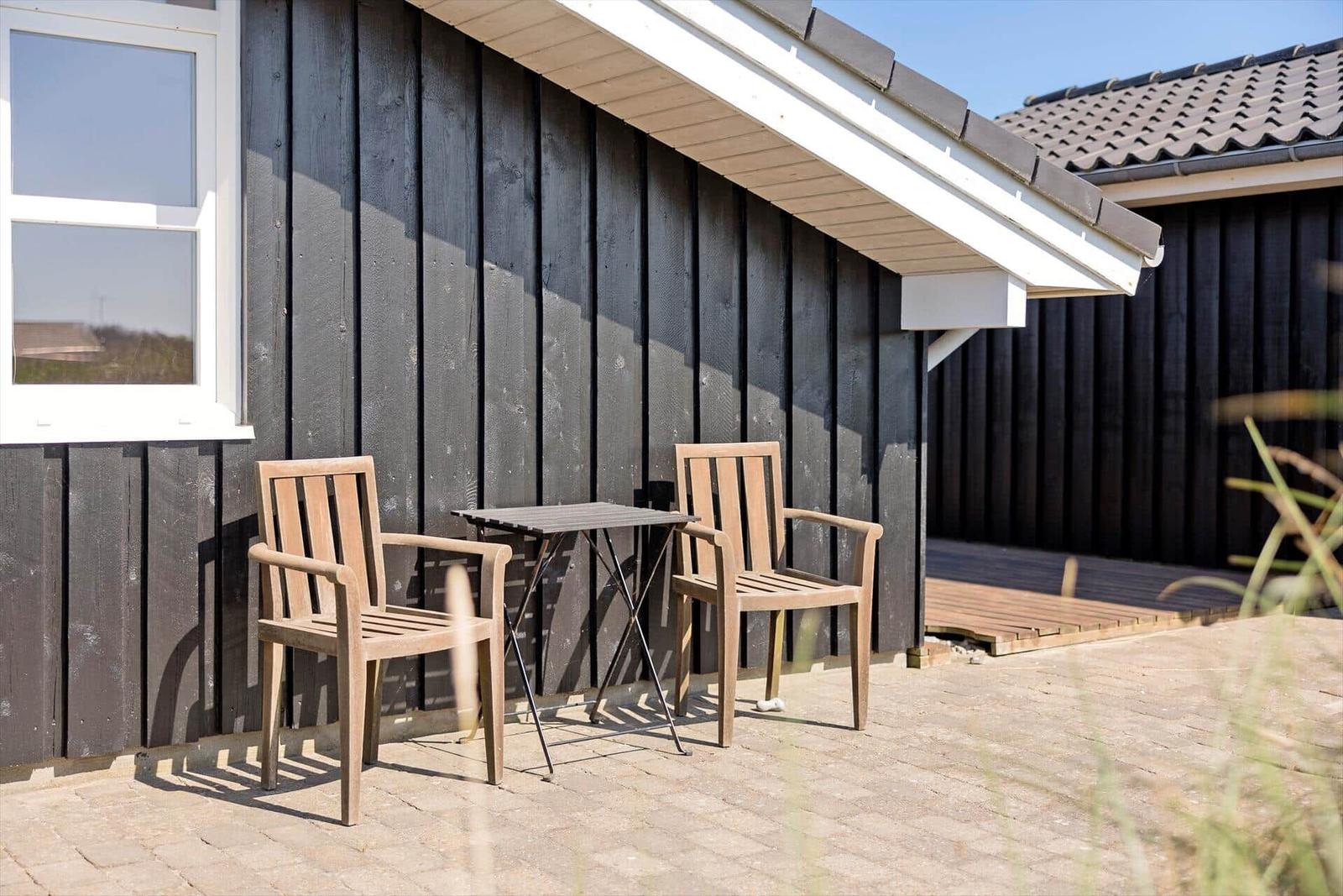 Terrasse mit Tisch und zwei Stühlen vor einem Haus mit dunkler Holzfassade.