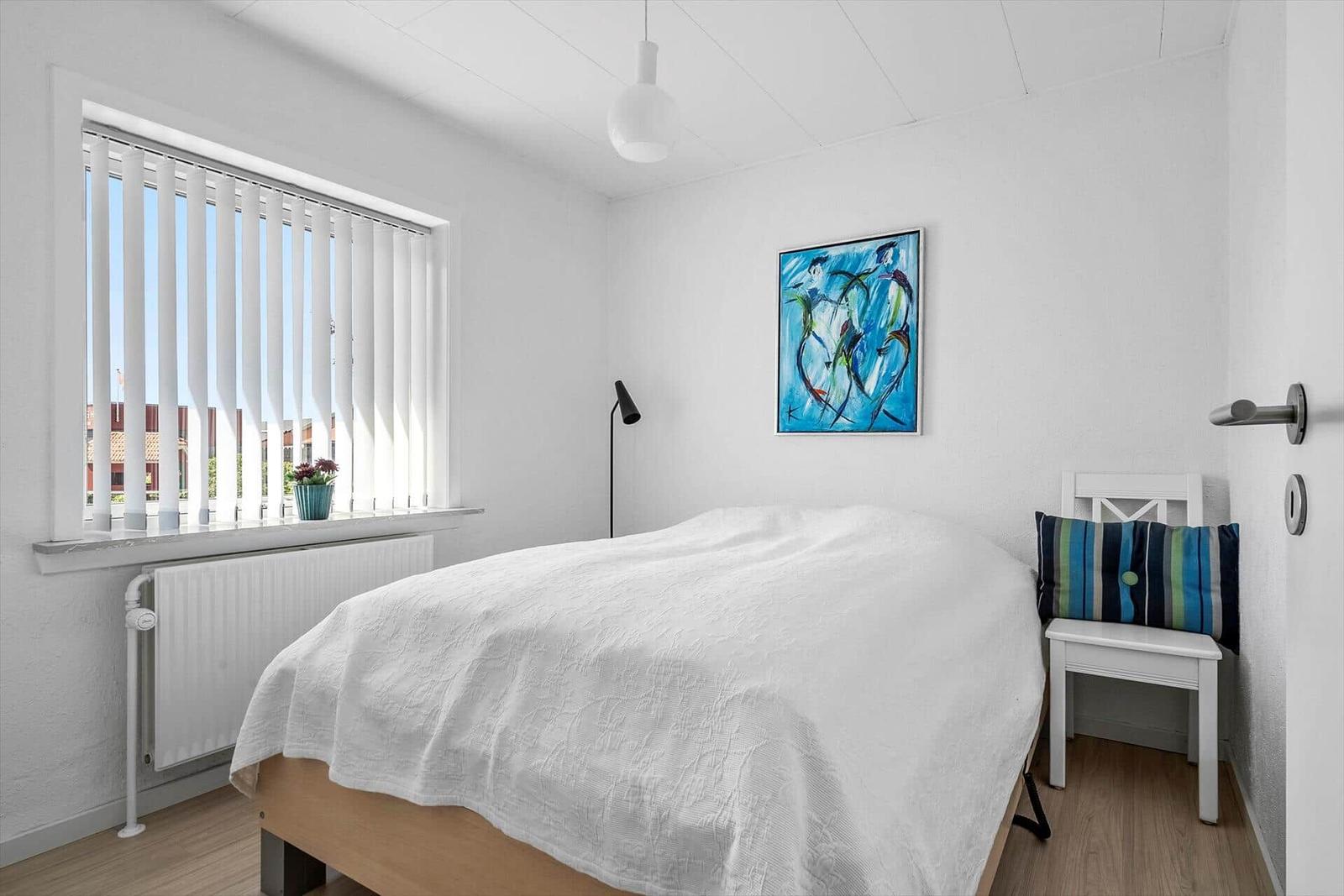 Schlafzimmer mit weißer Bettwäsche, Fenster mit Jalousie und Wandbild.