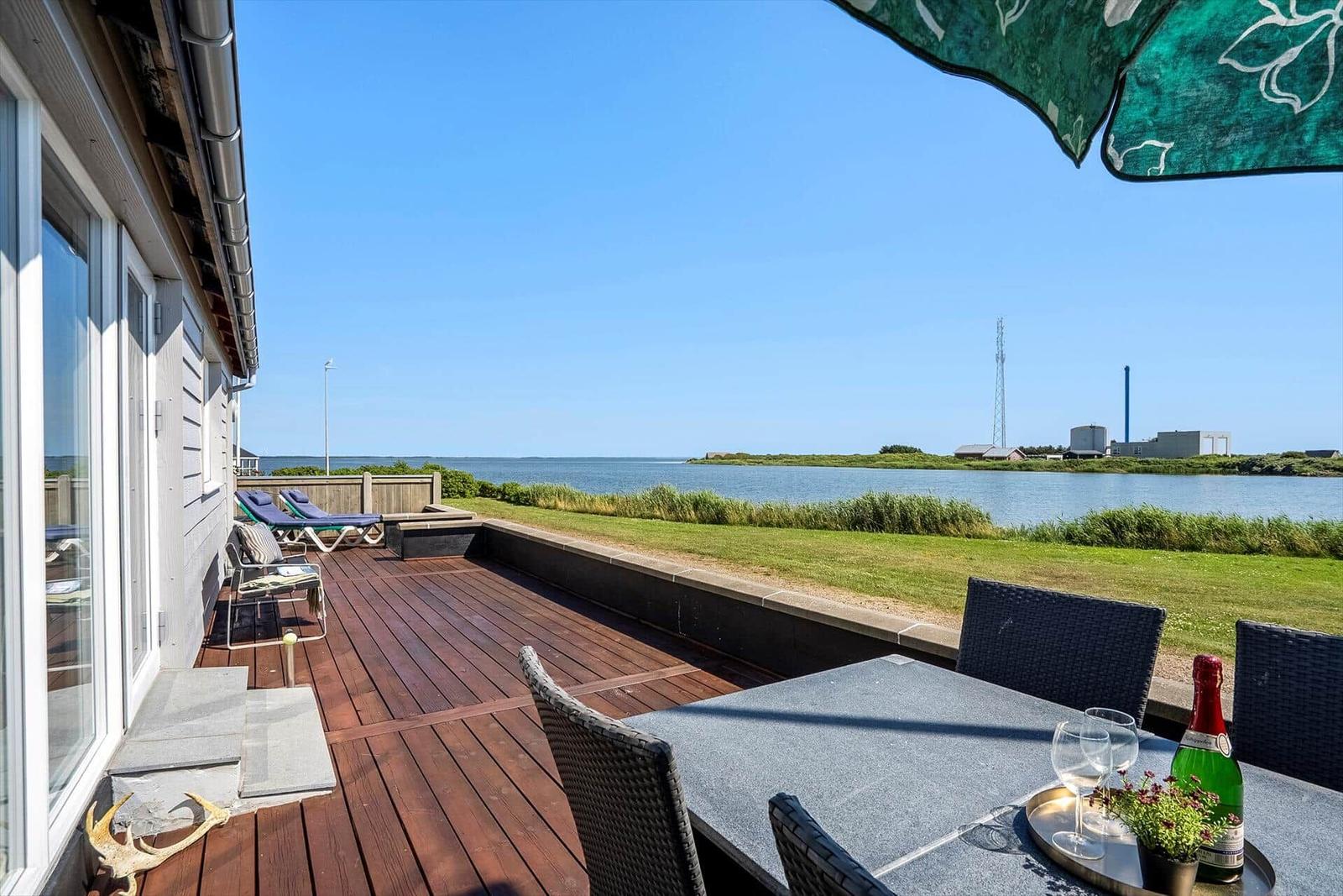 Terrasse mit Sitzgelegenheiten und Blick auf Wasser und Grasland.