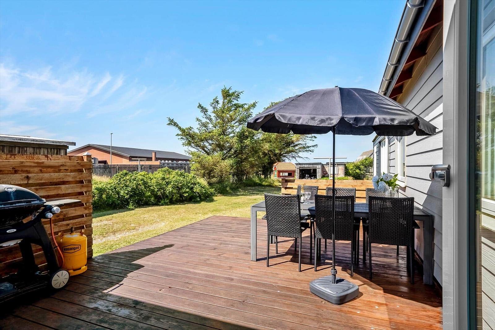 Terrasse mit Tisch, Stühlen und Sonnenschutz. Grill und Garten sind sichtbar.