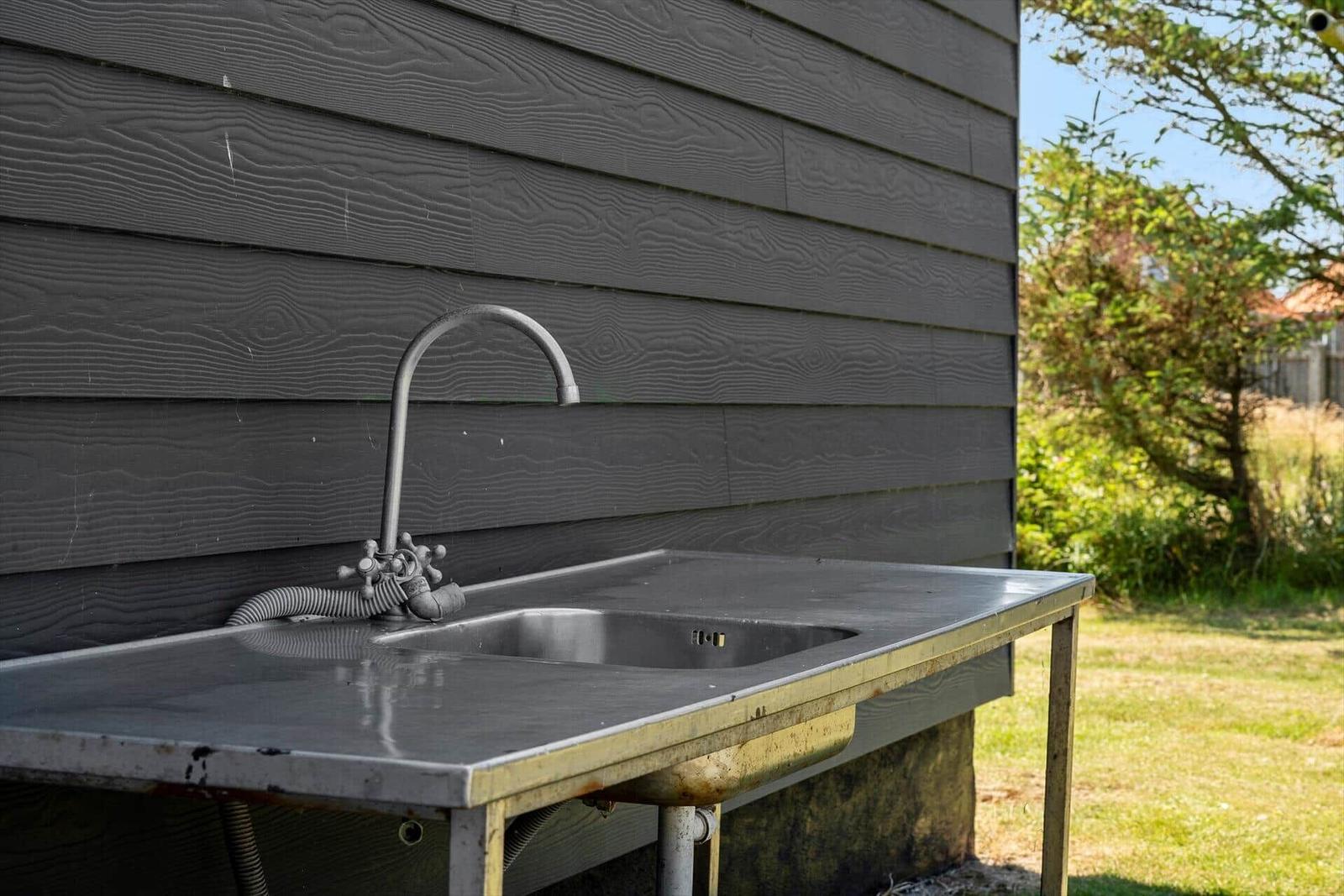 Außenwaschbecken mit Armatur an grauer Holzhauswand