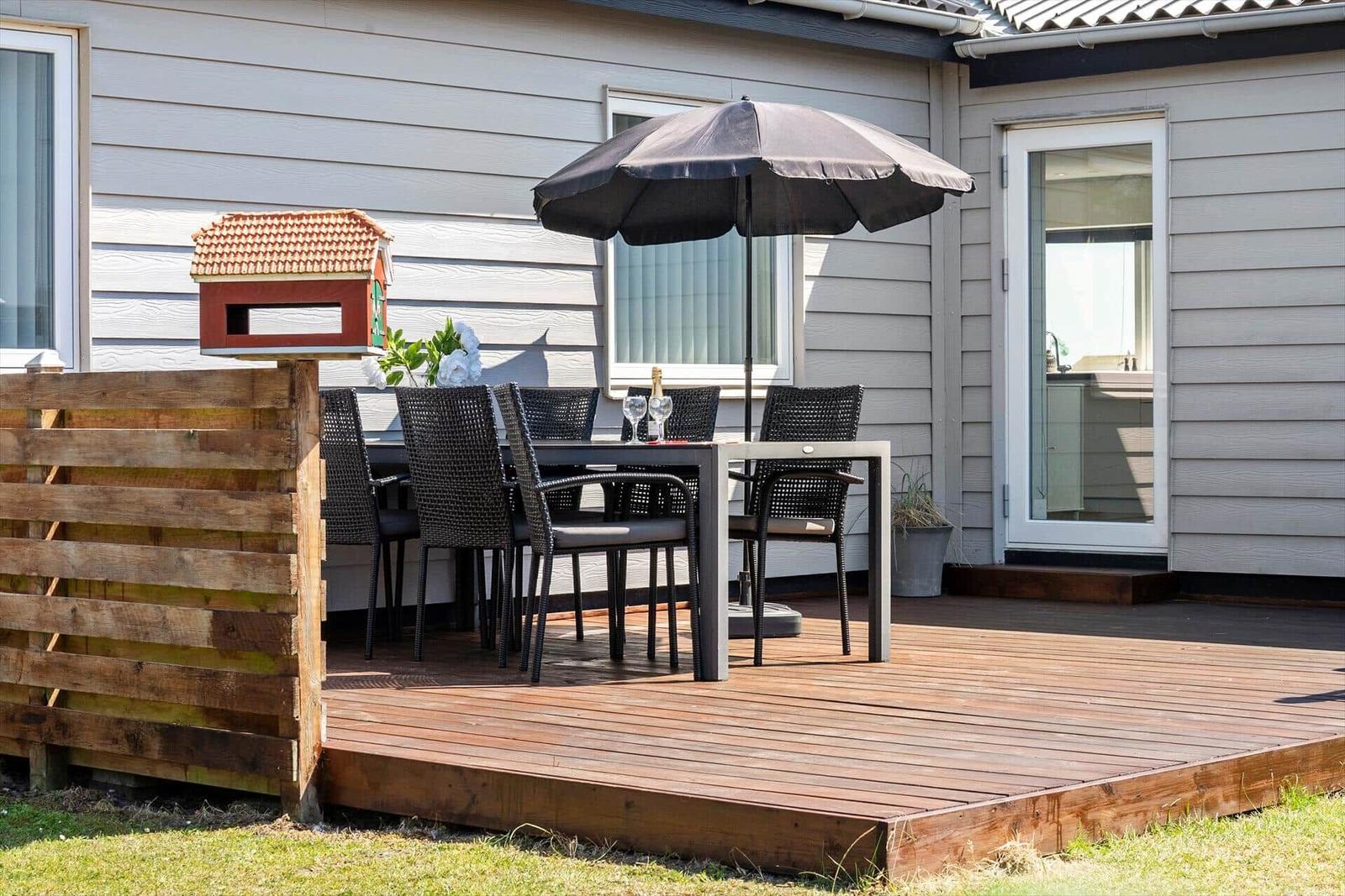 Terrasse mit Tisch, Stühlen und Sonnenschirm. Holzgeländer und Vogelhaus sichtbar.