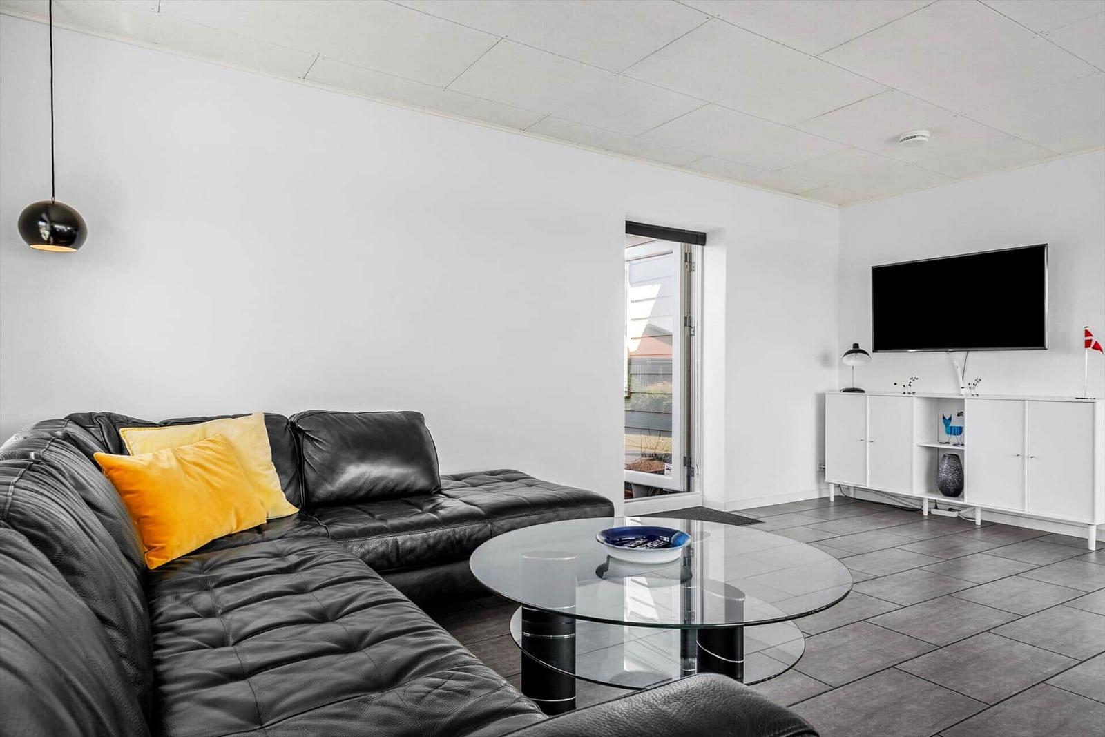 Schwarzes Ledersofa mit gelben Kissen, Glas-Tisch und Fernseher an der Wand.