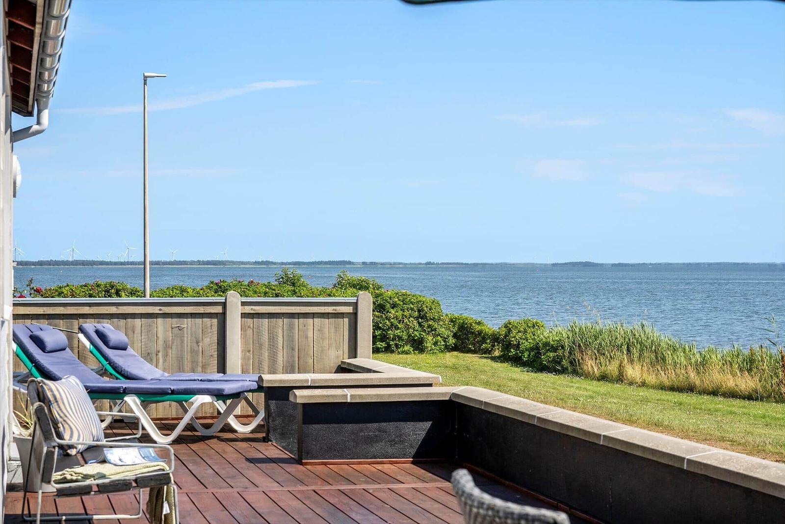 Terrasse mit Liegestühlen und Blick aufs Wasser und Windräder.