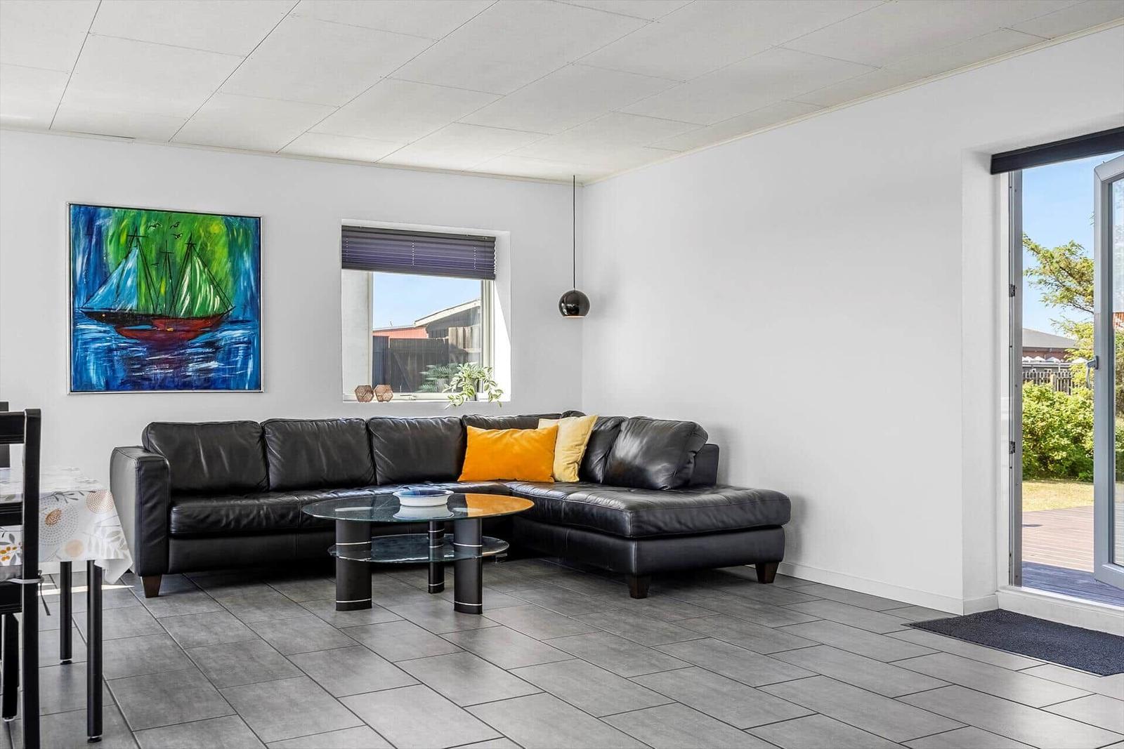 Schwarzes Ledersofa mit orangefarbenen Kissen, Glas-Tisch und Wandbild mit Segelschiff.