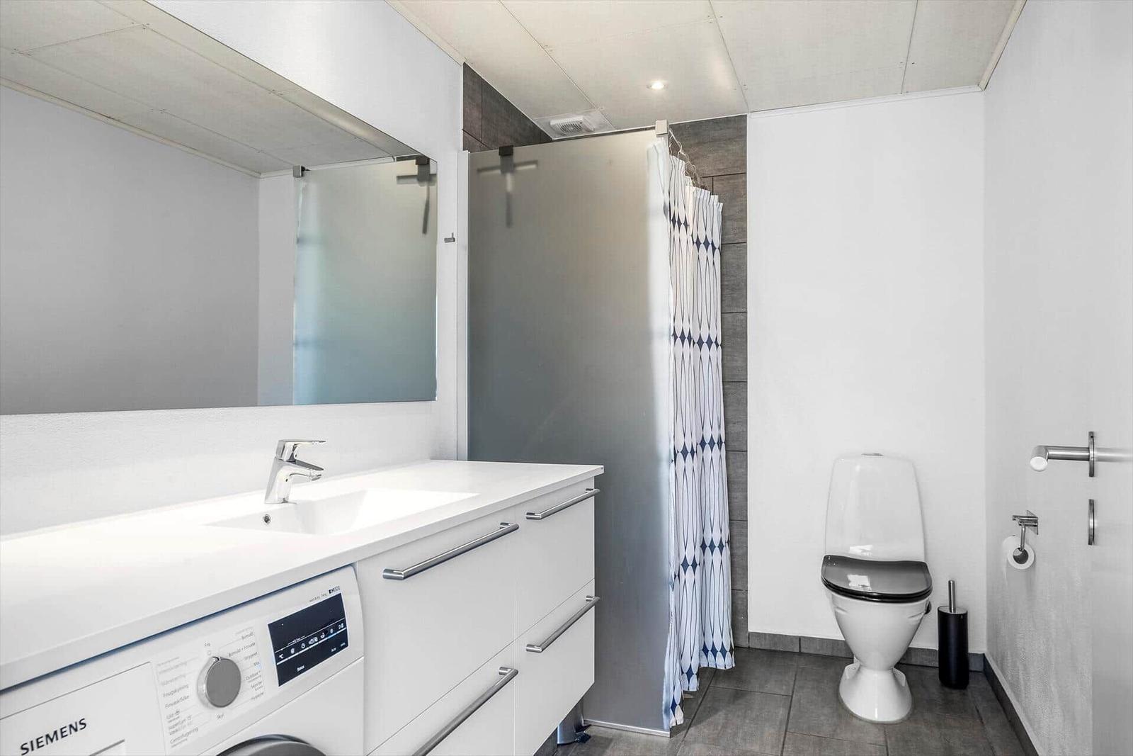 Badezimmer mit Waschmaschine, Dusche und Toilette.