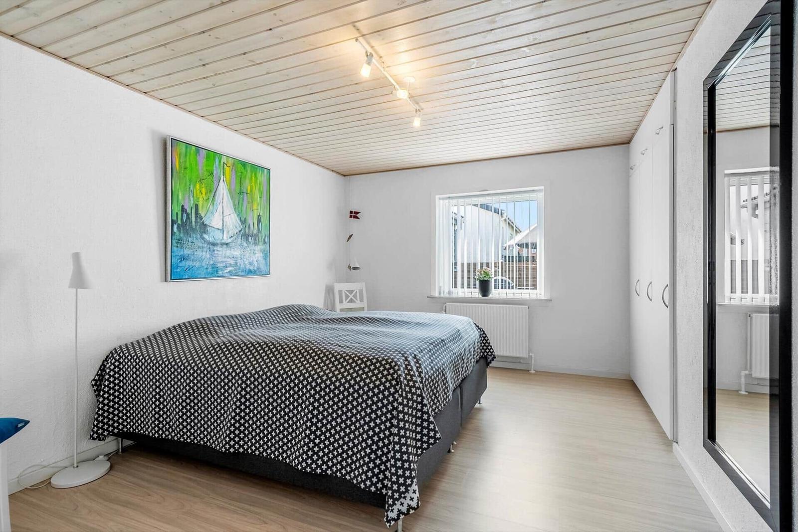 Schlafzimmer mit Bett, Wandbild und Fenster. Holzdecke und Kleiderschrank sichtbar.