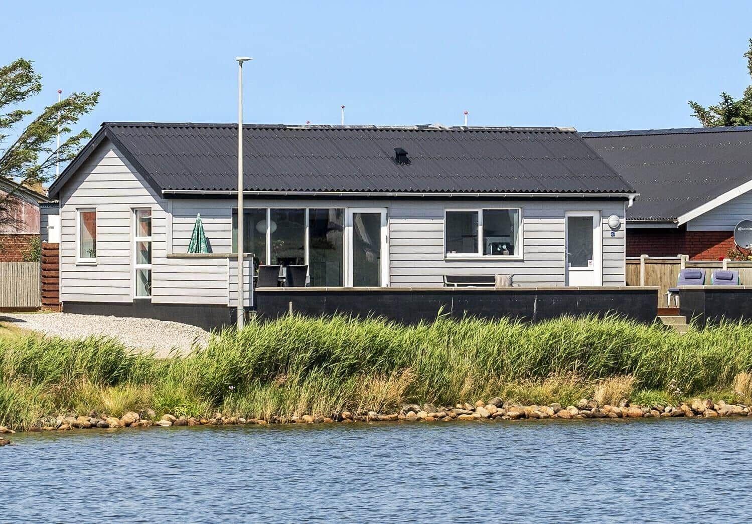 Ein Haus mit Terrasse direkt am Wasser. Fenster und Türen sind sichtbar.