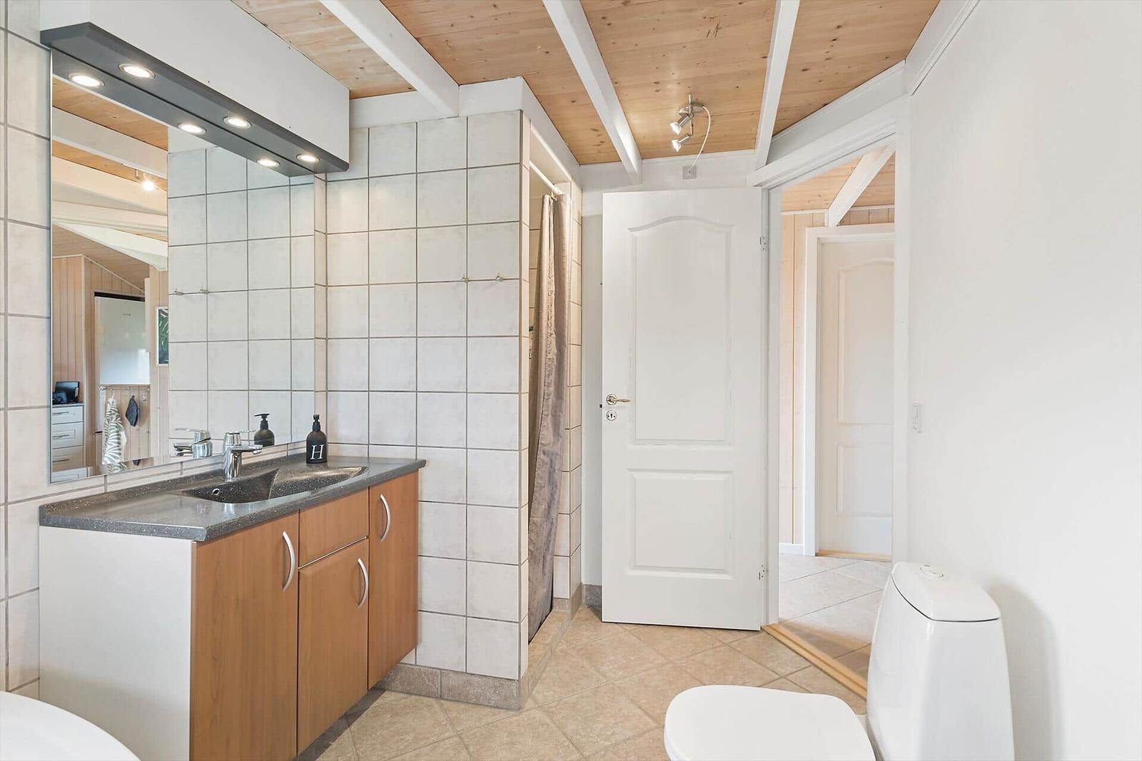 Badezimmer mit Waschbecken, Spiegel, Dusche und Toilette. Holzdecke und Fliesen.