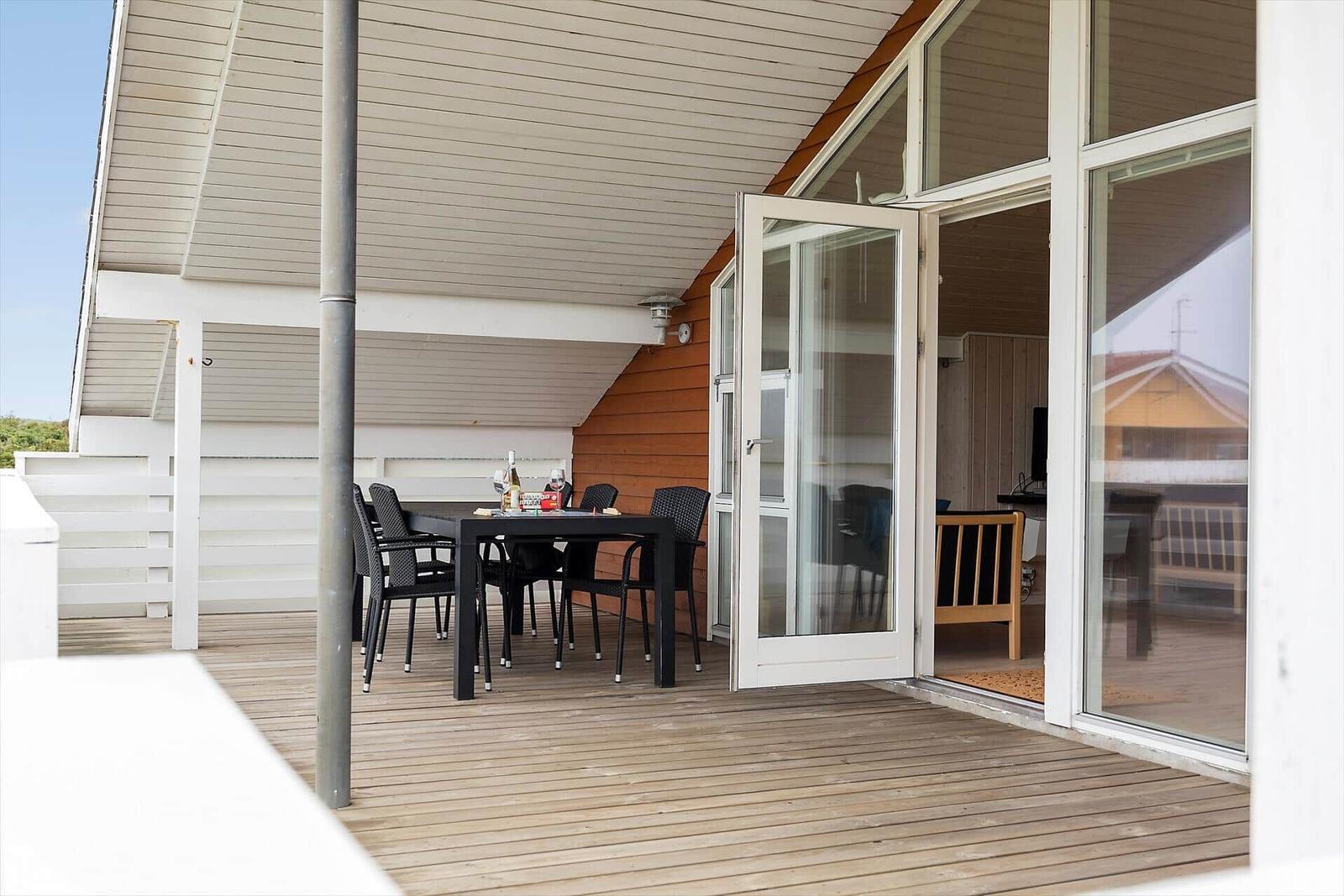 Terrasse mit Tisch und Stühlen, Zugang zum Innenraum durch Glastüren.