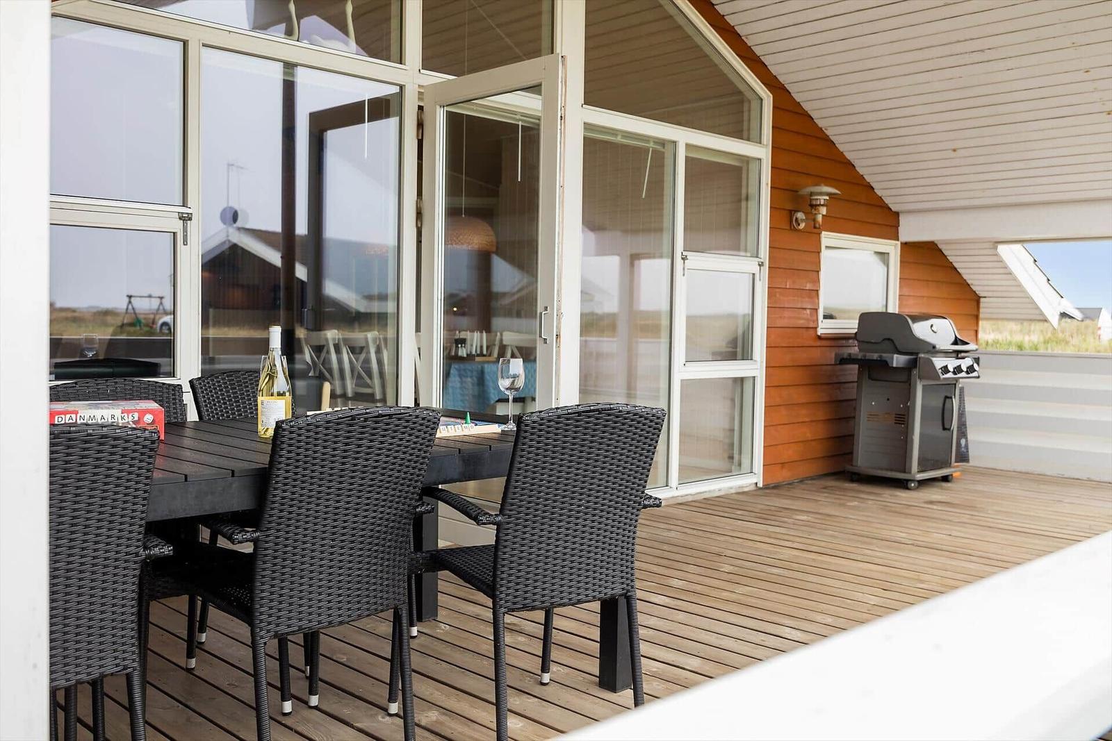 Terrasse mit Tisch, Stühlen und Grill. Durchgehende Glasfront zum Innenraum.